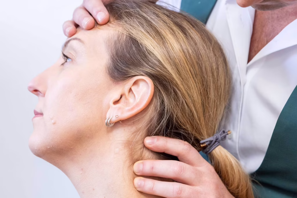 Chiropractor carrying out cervical disc palpation and neck examination on a female patient during a chiropractic assessment in Surbiton, UK.