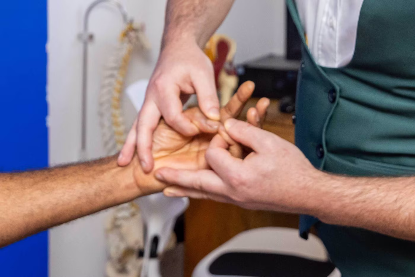 Chiropractor performing hand muscle testing on a patient’s wrist and fingers during a clinical assessment at a chiropractic clinic in Surbiton.