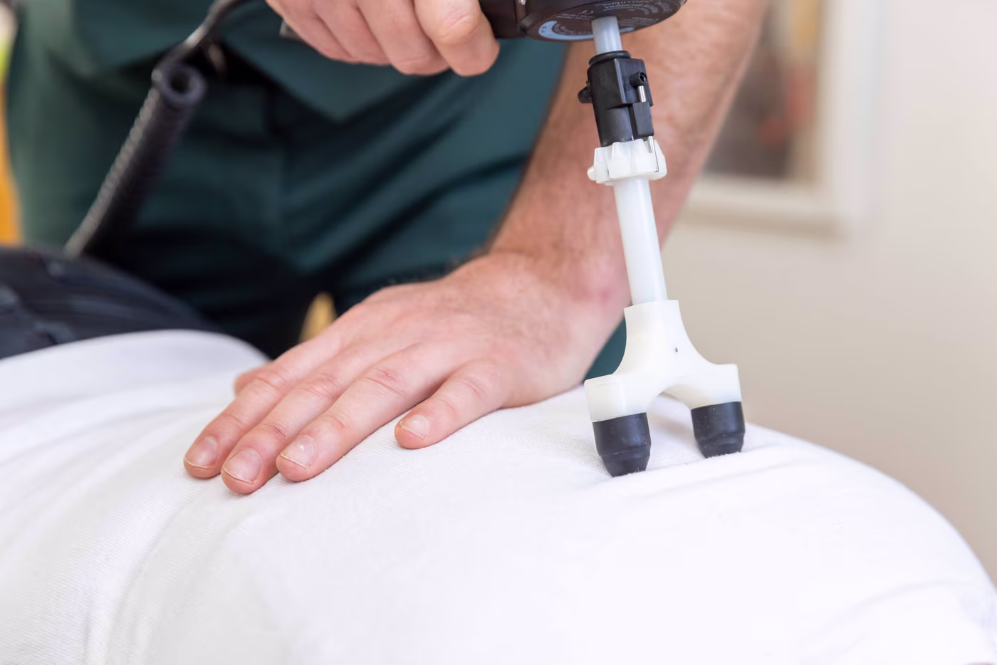 Instrument-assisted chiropractic adjustment being performed on a patient’s lower back using a handheld percussion tool at a chiropractic clinic in Surbiton.