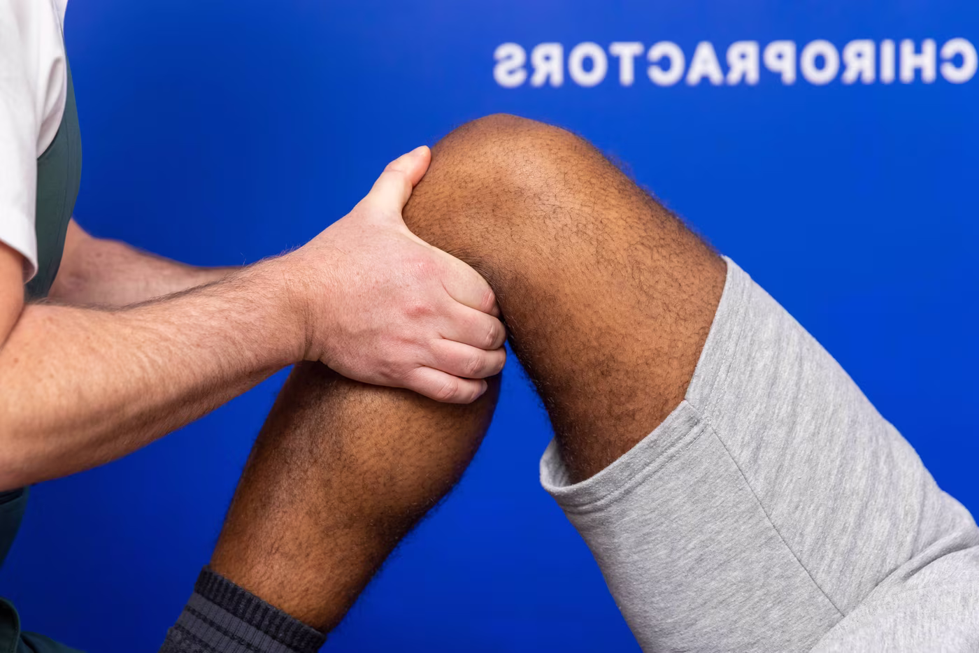 Chiropractor performing a knee ligament stability test on a patient’s bent knee during a clinical assessment in a chiropractic clinic.