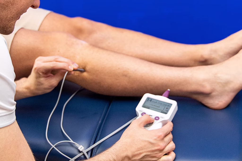 Leg nerve Stimpod therapy treatment in Surbiton, showing a chiropractor using a handheld neuromuscular stimulation device on a patient’s lower leg to help relieve nerve pain, sciatica and muscle dysfunction.