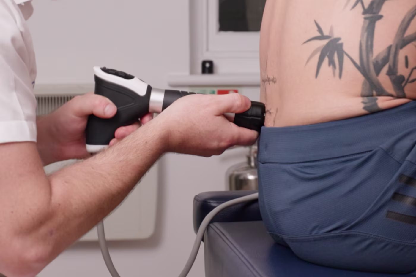 Lower back shockwave therapy treatment in Surbiton, showing a chiropractor using a handheld pressure wave device on a patient’s lower back to aid recovery from disc-related pain and sciatica.