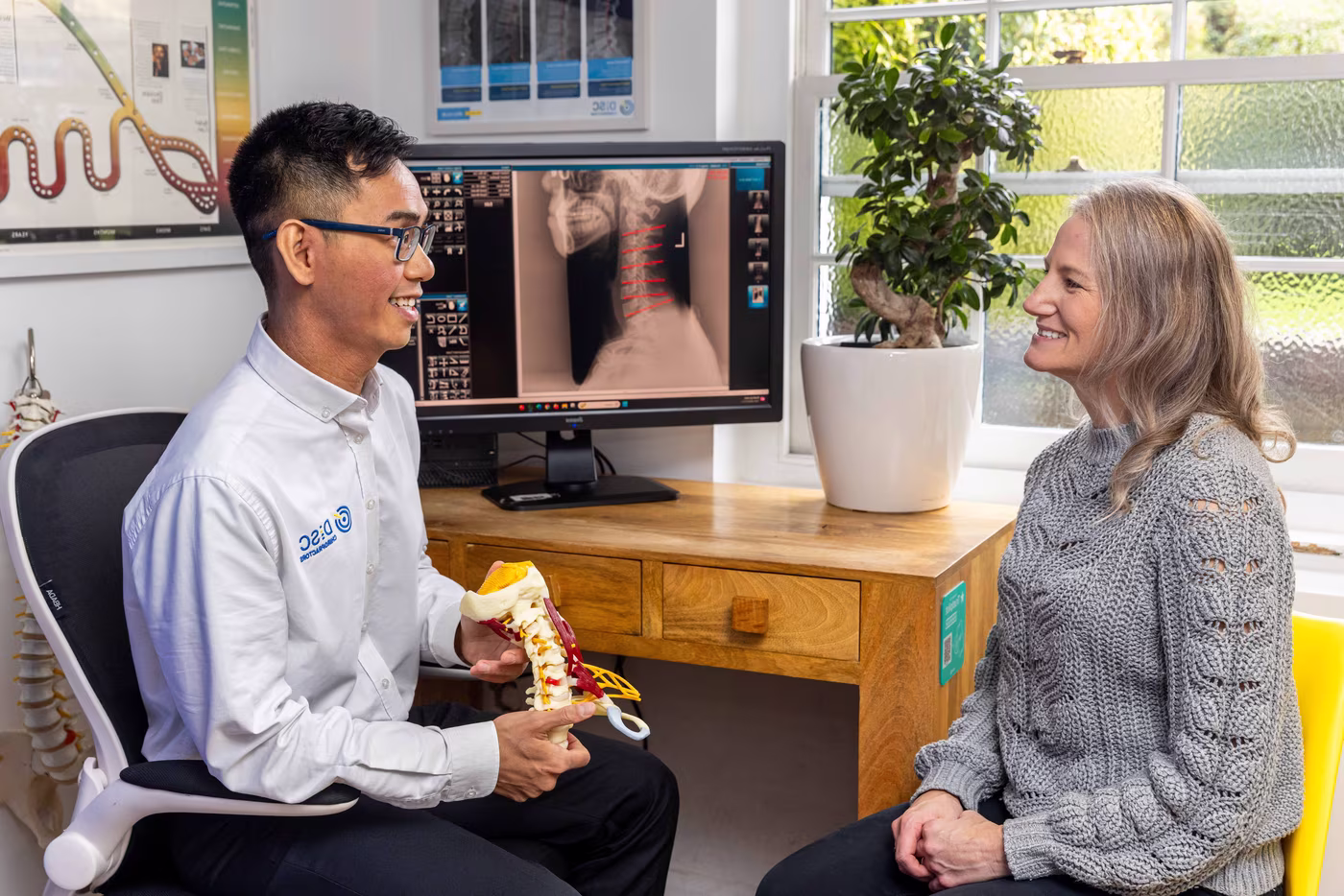 Experienced chiropractor explaining a patient’s neck X-ray during a new patient consultation at a specialist chiropractic clinic in Surbiton, using a spine model to discuss treatment and spinal health.